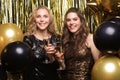 Two young ladies drinking champagne. Image of girls with balloons  on gold background Royalty Free Stock Photo