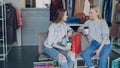 Two young ladies sitting in clothes department in mall and talking after shopping. Colourful women's garments and