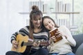 Two young lesbians are playing music. guitar and kalimba on the sofa in the living room