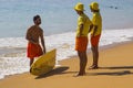 Two young lifeguards chat to a surfer at the waters edge on the beach at Albfueria in Portugal