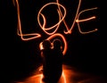 Two young lovers paint a heart on fire. Silhouette of couple and Love words on a dark background