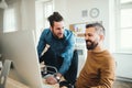 Two young male businesspeople with computer talking in a modern office. Royalty Free Stock Photo