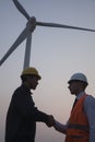 Two young male engineers standing beside a wind turbine at sunset and shaking hands Royalty Free Stock Photo