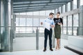 Two young architects with blueprints standing in office, talking. Royalty Free Stock Photo