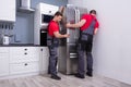 Two Young Male Movers Placing Steel Refrigerator In Kitchen Royalty Free Stock Photo