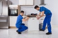 Two Movers Placing Dishwasher In Kitchen Royalty Free Stock Photo