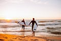 Two young male surfers in black wetsuits with longboards going to water at sunset ocean. Water sport adventure camp and Royalty Free Stock Photo