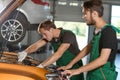 Two young mechanics in green overalls try to fix the engine of a Royalty Free Stock Photo