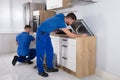Two Men Fixing Induction Stove And Sink Pipe In Kitchen Royalty Free Stock Photo