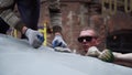 Two young men fixate grey tarpaulin to dome with white plastic loop pins.