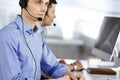 Two young men in headset, sitting at the desk in the modern office, listening to the clients. Call center operators at Royalty Free Stock Photo