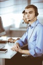 Two young men in headset, sitting at the desk in the modern office, listening to the clients. Call center operators at Royalty Free Stock Photo