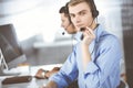 Two young men in headset, sitting at the desk in the modern office, listening to the clients. Call center operators at Royalty Free Stock Photo