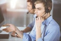 Two young men in headset, sitting at the desk in a sunny modern office, listening to the clients. Call center operators Royalty Free Stock Photo