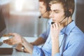 Two young men in headset, sitting at the desk in a sunny modern office, listening to the clients. Call center operators Royalty Free Stock Photo