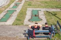 Two young men wearing Novi beograd tshirts in front of Abandoned mini golf course with decaying and rusting golf holes.