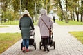 Two young moms girlfriends are walking with young children in strollers for an autumn Park. Women on a walk with the kids, the vie