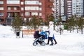 Two young mothers walk with their children in strollers along a winter snow-covered street in a residential area Royalty Free Stock Photo