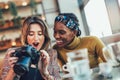 Young multiethnic women drinking coffee and lokking photo in photo camera in cafe