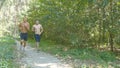 Two young muscular athletes running at the forest path. Active strong men training outdoors. Fit handsome athletic male
