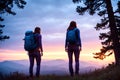 Two young non recognizable trekking woman with backpacks standing on top of mountain at sunset and enjoying view. AI