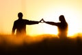 Two young people in love holding hands with shape of heart. Nature scenery, silhouette in rye, wheat field during summer sunrise