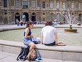 Two young person man and woman rest and sunbathe near the fountain on the square in front of the Louvre in Paris