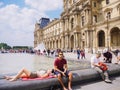 Two young person man and woman rest and sunbathe near the fountain on the square in front of the Louvre in Paris