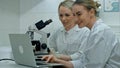 Two young positive scientists working in laboratory using microscope and laptop Royalty Free Stock Photo