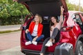 Two girls in trunk of red car posing for camera