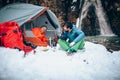 Two young professional male tourists are preparing food and hot drinks in the mountains near the river in winter.