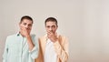 Two young scared twin brothers covering mouth with hand and looking at camera with shocked face expression while