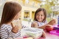 Two young schoolgirls eating packed lunch looking each other Royalty Free Stock Photo