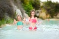 Two young sisters bathing in natural swimming pool in Bagno Vignoni, with thermal spring water and waterfall. Tuscany, Italy