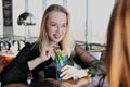 Two young smart beautiful girls in dresses sit at a restaurant table opposite a large window. Drink red and blue Royalty Free Stock Photo