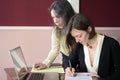 Two young smartly dressed women filling out forms at a vintage office desk in front of a laptop Royalty Free Stock Photo