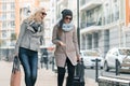 Two young smiling beautiful women in warm clothes walking down the city street with a travel suitcase, women laughing and talking Royalty Free Stock Photo