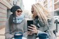 Two young smiling fashionable women having fun in outdoor cafe. Urban background, women laughing looking at mobile phone Royalty Free Stock Photo