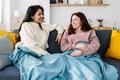 Two young smiling latin american women covered with a blanket talking on sofa Royalty Free Stock Photo