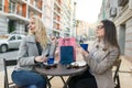 Two young smiling women in an outdoor cafe, drinking coffee, talking, laughing. Urban autumn background Royalty Free Stock Photo