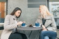 Two young smiling women in an outdoor cafe, drinking coffee, talking, laughing. Urban background Royalty Free Stock Photo