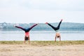 Two young strong sportswomen, wearing colorful fitness outfits, doing cartwheel exercise outside by city lake in summer. Street Royalty Free Stock Photo