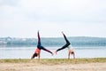 Two young strong sportswomen, wearing colorful fitness outfits, doing cartwheel exercise outside by city lake in summer. Street Royalty Free Stock Photo