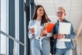 Two young student friends together in a corridor of a college walking together and holding notepad, laptop and cup of Royalty Free Stock Photo