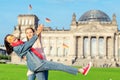 Young student girls having fun and dancing and piggybacking on the grass near famous landmark in Berlin - Bundestag building.