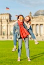 Young student girls having fun and dancing and piggybacking on the grass near famous landmark in Berlin - Bundestag building.