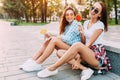 Two young stylish women sitting on a skateboard with lollipops happily smiling. enjoy a Sunny day in the city