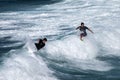 Two surf riders re-enter the crest of a wave