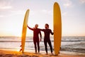 Two young surfers in black wetsuit with yellow surfing longboards on a ocean coast at sunset ocean. Water sport Royalty Free Stock Photo