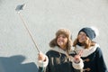 Two young teenage girls having fun outdoors, happy smiling girlfriends in winter clothes taking selfie, positive people and Royalty Free Stock Photo